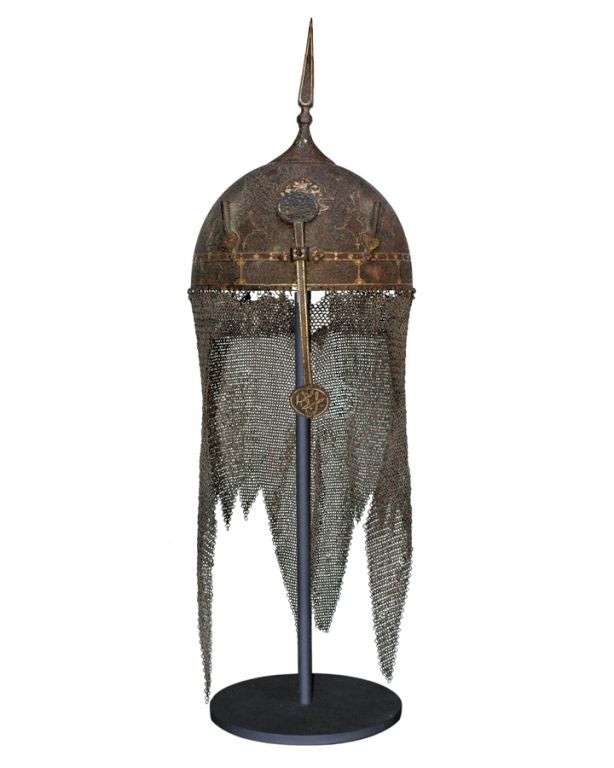 AN EXOTIC PERSIAN SPIKED STEEL HELMET WITH GOLD HIGHLIGHTS AND SLIDING  NASAL PLUME WITH CHAIN MAIL COWLING. The circular domed helmet; the apex fixed with the slender, four-sided, tapered spike raised above a spheroid element on the flaring