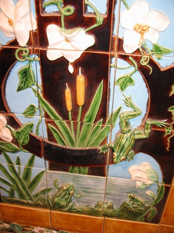 A nice large and bright majolica pottery tile panel depicting jumping frogs in a pond with cattails and flowering vines.  The ochre colored border is framed by a garland of frogs and flowers.  The panel gives the impression of a stained glass