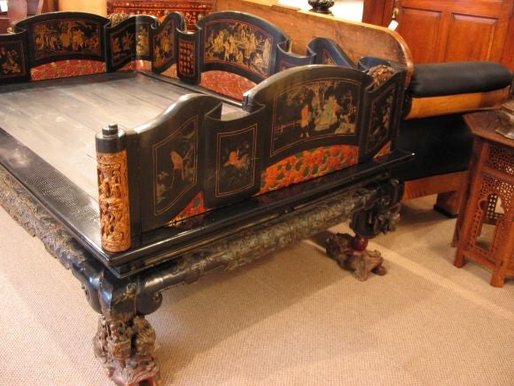Elaborate carved lacquered and gilt opium bed.  Decorated all over with poems, animals and paintings of figures in pavillions.  The bed stands on four carved and painted foo dogs.  The back rail carved as unrolling scroll.