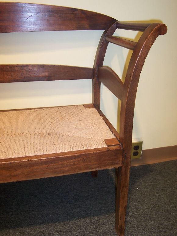 Simple, yet elegant, antique French rushed seat bench with curved arms.