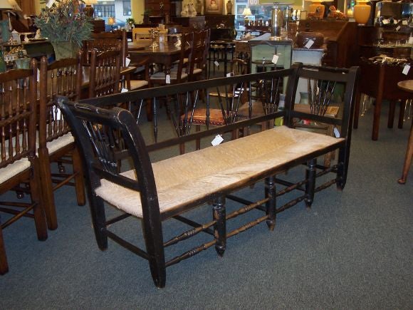 Antique bench from France painted black with a rush seat. Unusual spindle rails. The paint has nice wear and patina. Good larger size with four seats.