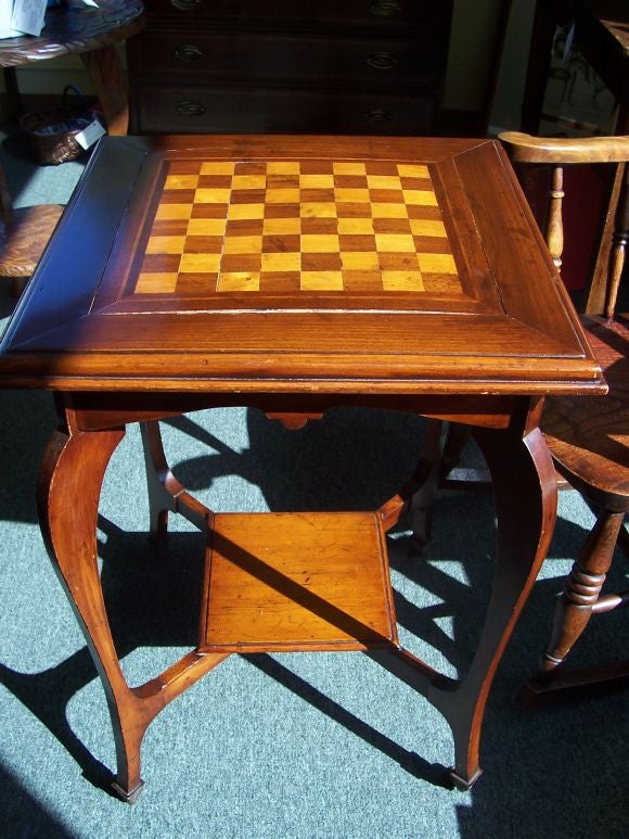 Antique English chess table with inlay. The mahogany has a rich warm finish. Gracefully curved legs on castors with a small shelf below. There has been some restoration to the top, and some separation has occured on the inlay.