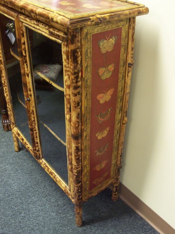 Antique bamboo cupboard from England. Newly decoupaged with butterflies on a crackled red surface on the top and sides. Two glass front doors open up to two shelves with bamboo detail.<br />
<br />
This cabinet is currently in our Southampton