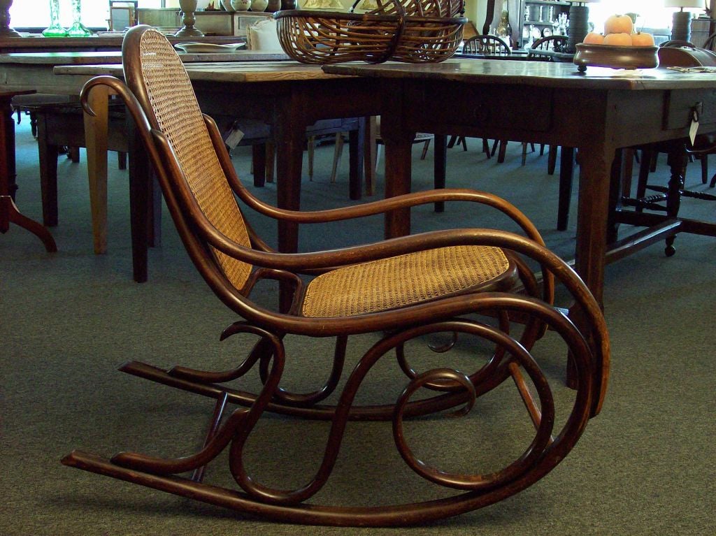 Antique Thonet rocker. The color of the bentwood is deep and has a lovely patina. Replaced cane is in very good condition. Note in image 3 the facing right arm is slightly warped, as is the seat.  From any other view, this is not noticable. Formerly