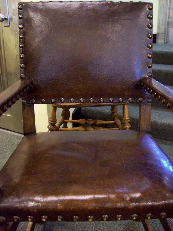 A pair of antique armchairs from England. The chocolate brown leather and the dark oak have a nice patina and are in very good condition. Beautifully turned bobbin stretchers on the fronts. These chairs are quite sturdy. Arm height is 27