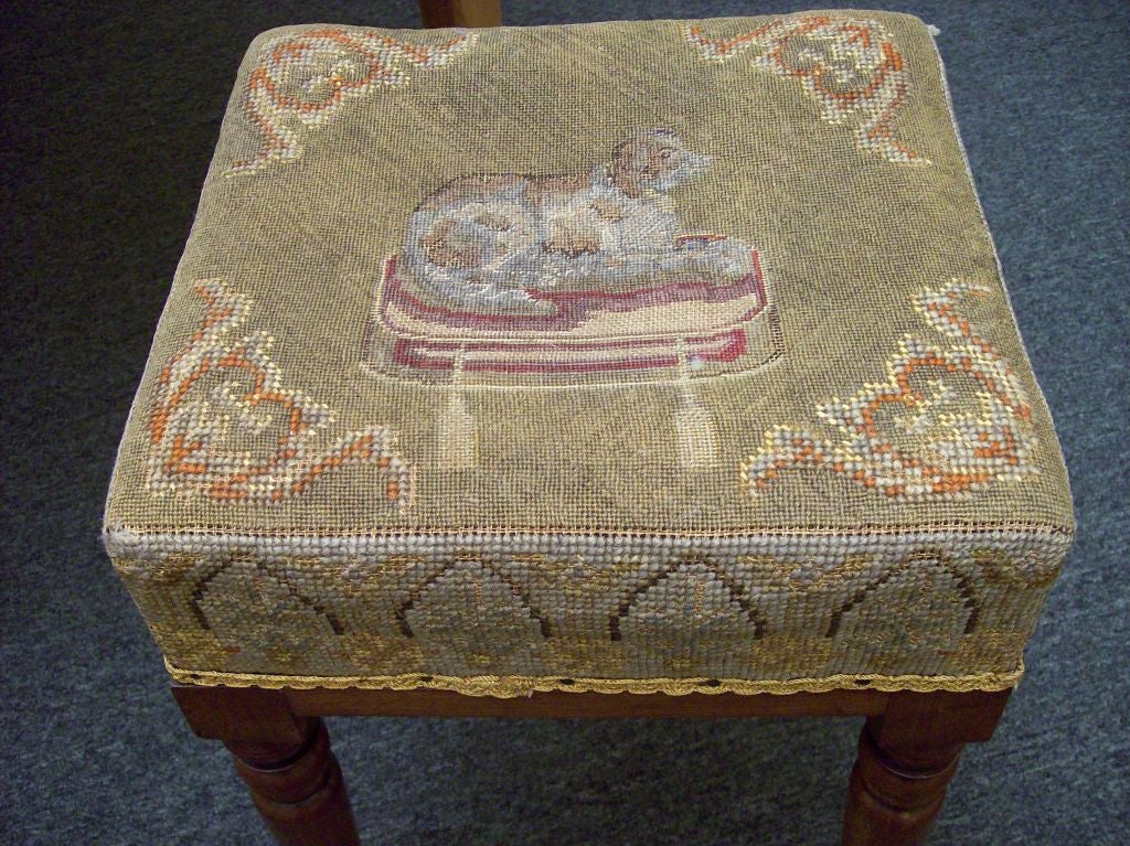 An antique English stool with needlepoint, perfect for any dog lover! The beautifully turned mahogany legs, square shaped top, and lovely needlepoint give this stool great charm. The needlepoint is no doubt later than the c1820 stool, but it is