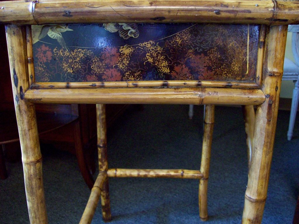 Small antique bamboo desk from England with one drawer. All four sides of the apron are decorated, either with hand painting or on the back with the wallpaper-type material typically used. The bamboo has a desirable, honey color to it, and the top