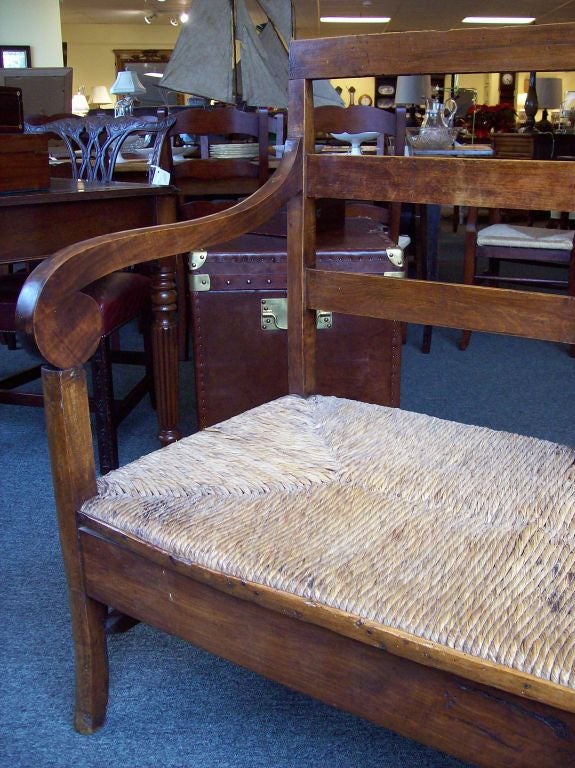 Large scale antique bench from France. This fabulous bench has a an old rush seat and scrolled arms. The fruit wood has wonderful color and patina. Very sturdy.