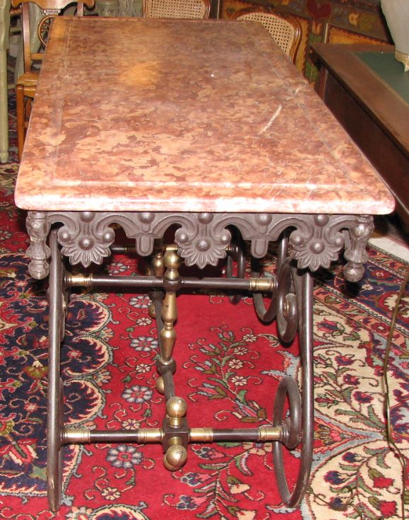 European reproduction of a butcher's table with marble top & solid iron base with brass accents; originally used around the 19th Century by a butcher shop in France.