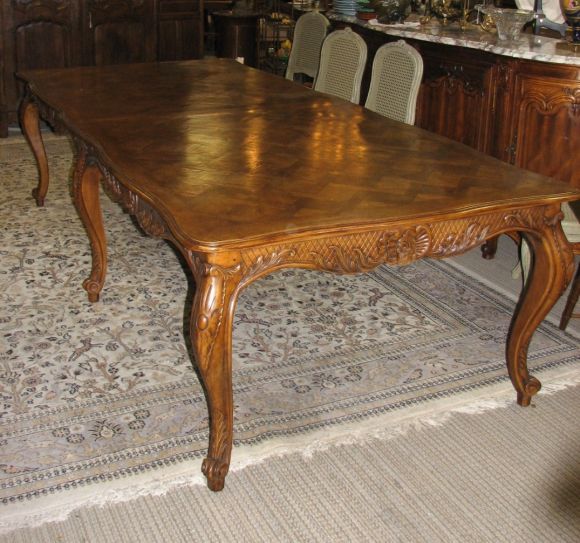 Reproduction Louis XV-Style inlaid parquetry top dining table with six (6) cabriolet legs (two at each corner of table and two at center sides). Legs are tapered and curved, with carvings. The table's apron is carved as well with a leaf, scalloped