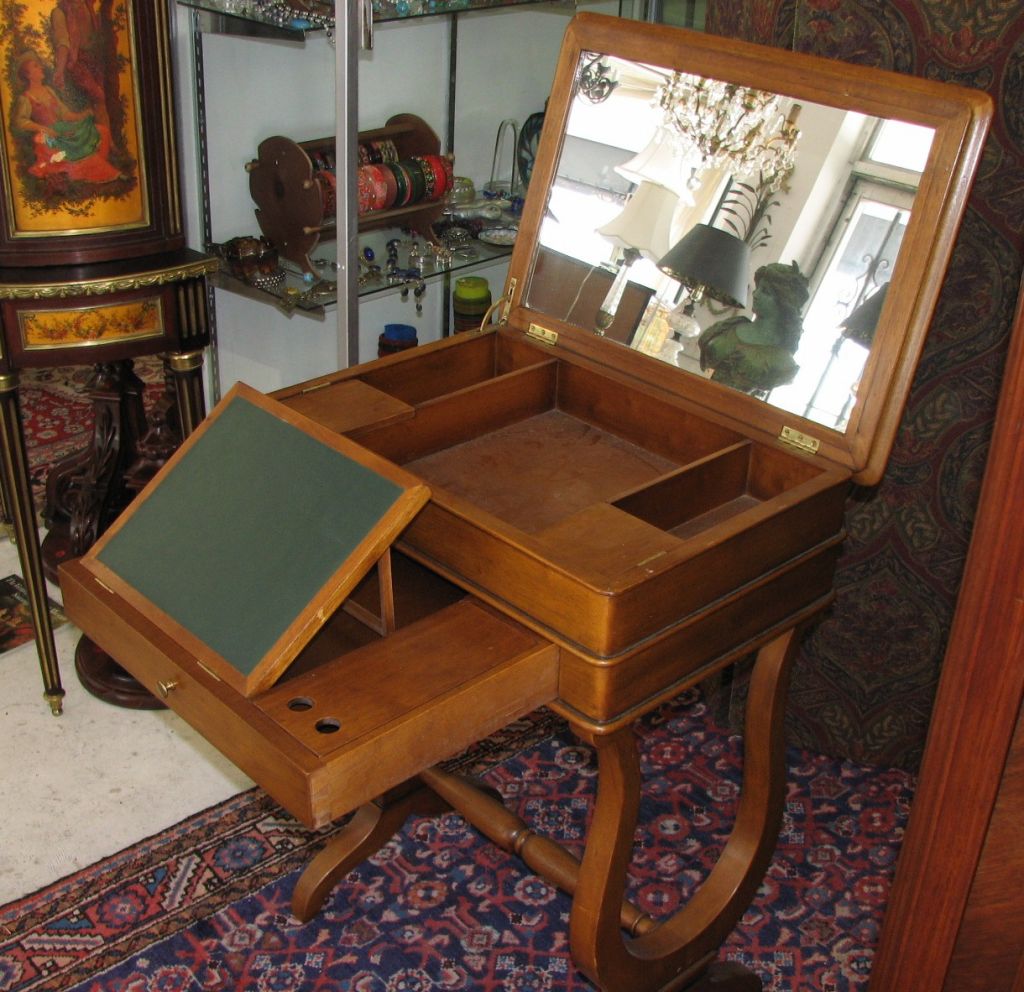 Compact fruitwood vanity/writing table with a pull-out drawer containing a leather-top, hinged flip-up writing tablet alongside a covered rectangular compartment. <br />
<br />
The lift top of this piece is mirrored on the underside and lifts to