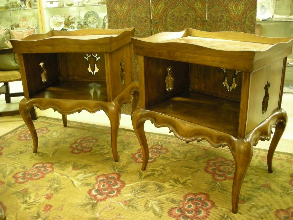Unusual pair of tables constructed of walnut wood with pink marble-top inserts. Scalloped apron and open work carvings on each of three sides of cubby hole storage area.