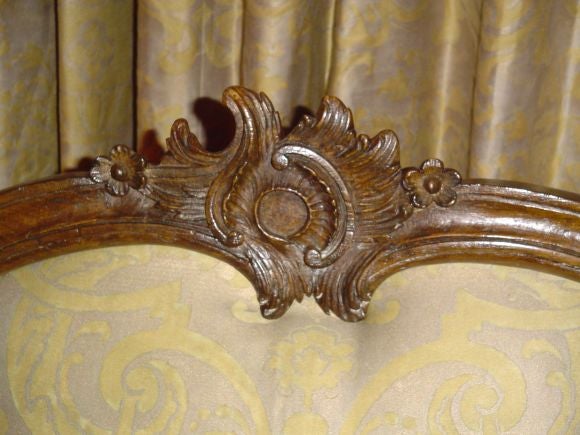 Unstamped or signed; carved and molded upholstered splat with attached sunflower-form crest highlighting a C-scroll and a floral bow at base center; carved, molded and upholstered arms with scrolled grips, and C-scroll acanthus-decorated arm