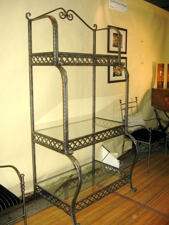 Iron and glass etegare/bakers rack with unusual fretwork surrounding each shelf.   Color of iron is a deep gunmetal.  Three glass shelves become progressively deeper.  Great form.