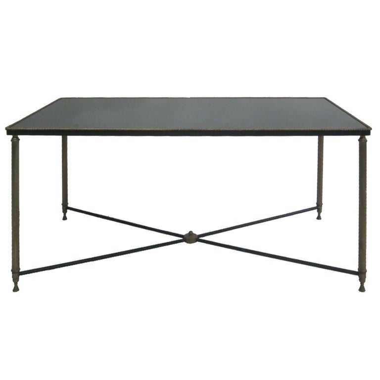 An elegant French Mid-Century coffee table with gilt metal legs and trim and a patinated black frame and stretcher. The table supports a top of dark grey mirror creating a chic effect. Maison Jansen.