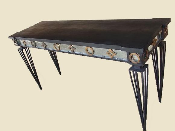 Chic 1940s style French consoles in the Mid-Century Modern Neoclassical taste of Gilbert Poillerat. The structure is in wrought iron with sharply tapering legs and with a mirrored apron featuring decoration with gilt circular and star forms. Stone