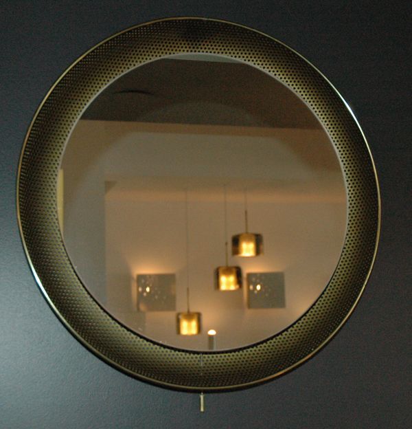 Perforated brass plated metal shell with ring of light illuminating the mirror and pull chains.  Mirror shows age around the circumference.