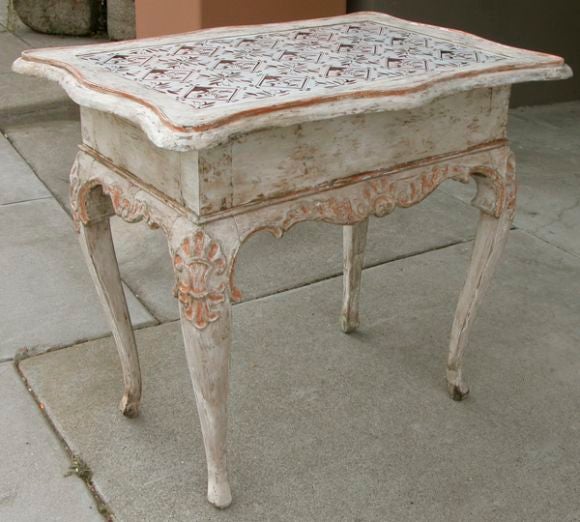 A graceful Danish rococo gessoed and ivory painted single drawer side table with coral painted highlights; the top inset with Dutch delft tiles depicting stylized floral stems