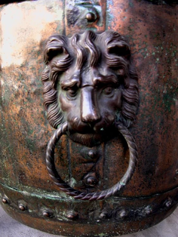 A large-scaled and handsome English copper coal/log bin with lion ring handles; the large cup-shaped body of patinated copper adorned with robust lion ring handles; raised on 3 curvaceous paw feet