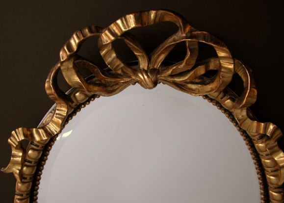 Un miroir ovale Napoléon III festif et de grande taille, en bois doré et ébénisterie, avec une crête de ruban sculpté ; le miroir ovale biseauté dans un cadre conforme de moulures en forme d'œuf et de fléchette avec un engobe perlé ; le tout