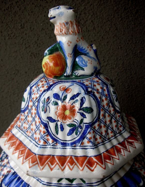 A massive Dutch polychromed tinglazed delftware lobed urn with lid surmounted by a regal lion; the domed lid topped by a fu lion; resting on a lobed tapering urn adorned with 4 reserves with exotic birds surrouned by floral and foliate motifs; with