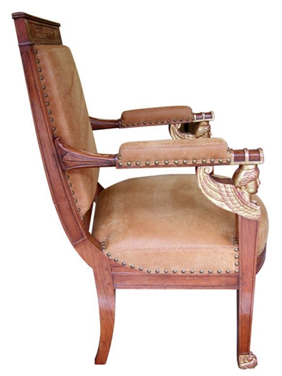 A good pair of French empire fruitwood and parcel-gilt armchairs with sphinx-head motifs; each with rectangular framed back above half-round padded arms emanating from lotus leaf carving; raised on well-carved winged sphinx heads above a bowed seat;