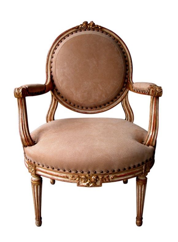 A large-scaled and elegant French Louis XVI style ivory painted and parcel gilt oval back open armchair; the circular padded back with floral carved crest rail above padded arms over s-scrolled supports; joining a generous bowed seat and apron with