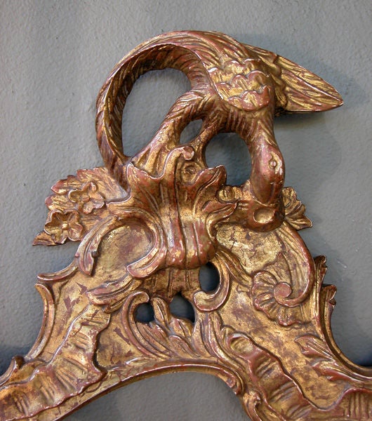 the original hand-beveled cartouche-shaped mirror plate within a conforming giltwood frame surmounted by a bold ho-ho bird; the whole adorned with elaborately stylized rocaille carving and scroll motifs; the Ho Ho bird was originally seen in asian