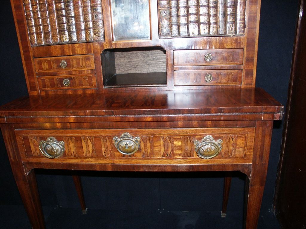Mahogany with Kingwood inlay Ladies Writing Desk with brass gallery around marble top faux book cabinet doors flanking mirror above small drawers on either side of cubby hole with secret compartment. The fold out leather writing surface above single