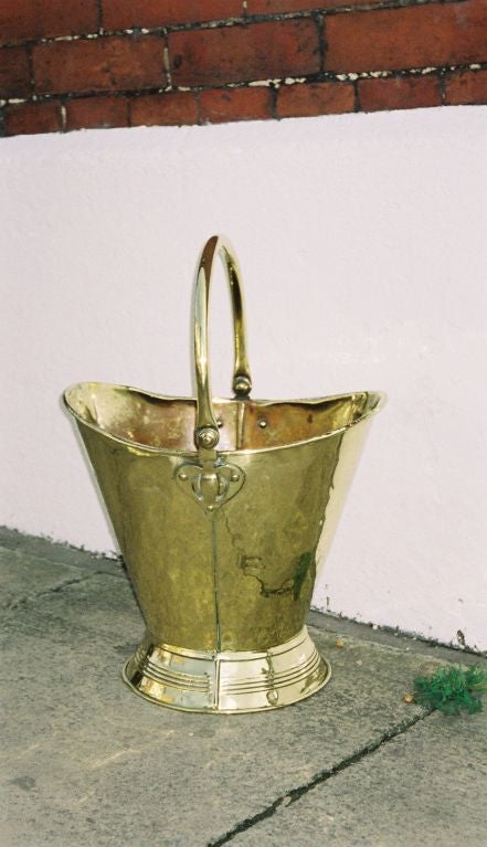 A 19th century English brass log basket with carrying handle ending in heart shaped pivot hinges