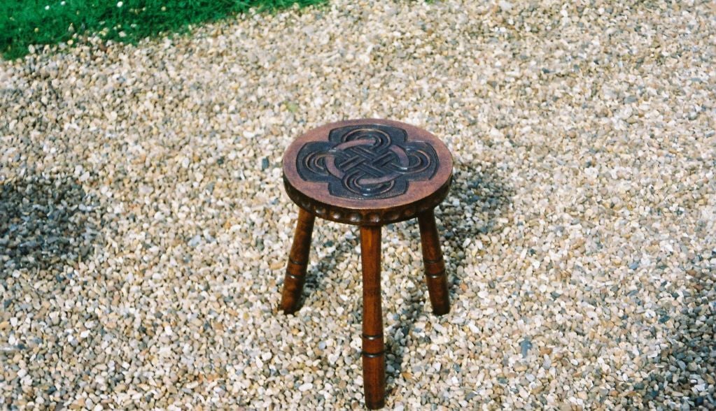 An English Arts and Crafts school three legged stool with turned legs having a round top with incised carving in the Celtic manner