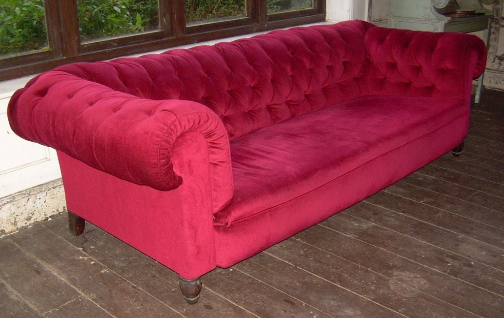 An English 19th century over-scale country house button back Chesterfield sofa in red velvet on turned mahogany legs.  Deep and comfortable.