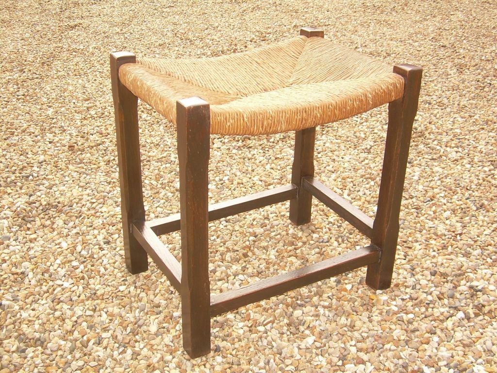 An English stool in oak with chamfered legs and stretcher base, having original woven rush on curved seat.