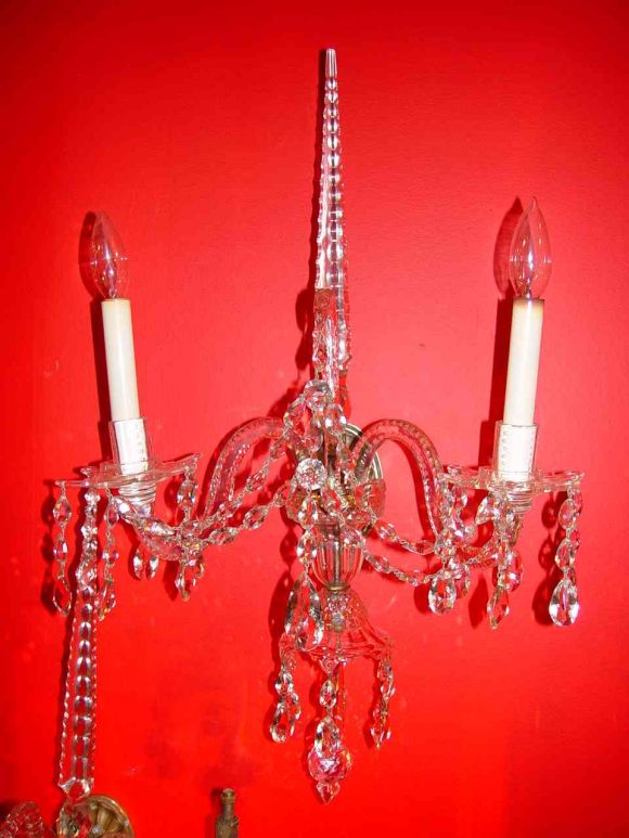 A fine pair of early George III crystal sconces with center spire over  two candelabra arms and swan neck center support, strung with pear drops. The cast brass backplates of typical fluted patera form. Later electrified.
