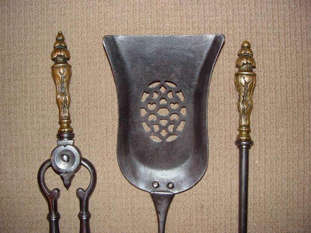 A fine set of three 19th Century English fire tools comprising shovel, poker and tongs, in gunmetal steel with cast gilt metal handles, shaped shovel with abstract cut-out decoration.