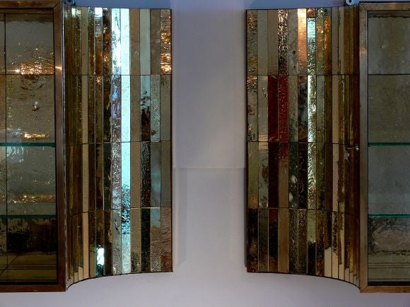 Stunning pair of French 1960's bronze and gold mirror tiled hanging cabinets with glass doors and shelves, covered entirely in rare striated and bubbled gilded glass mirror tiles. The cases with beautifully unique shaped flaired-curved ends. Each