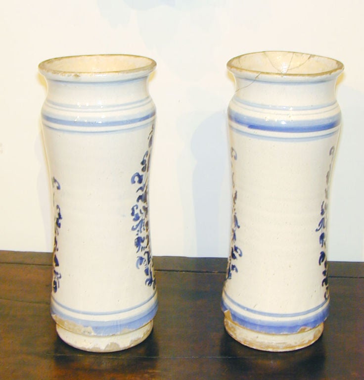 Pair of large Spanish Catalonian apothecary jars of waisted form with blue and white floral decoration.  One jar labeled, G LACCA, a resinous substance secreted by the lac insect. The other labeled, S CUBEB, a dried unripe fruits of the shrub piper
