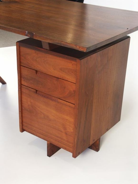 Excellent conoid desk by Nakashima 1970's. Black walnut construction throughout, with free edge desktop, with beautiful natural hole detail. Single three drawer pedestal, and Conoid leg support. Incredible Nakashima craftsmanship to every detail.
