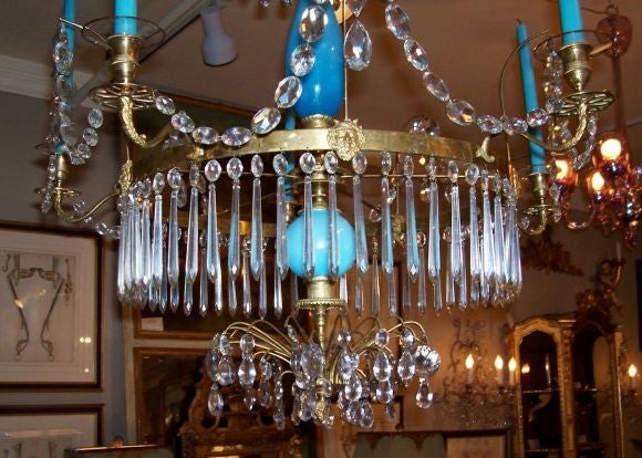 The tiered arching coronet above an opaline porcelain baluster form standard over a circular tier issuing five S-scrolled dolphin cast candle arms alternating with  masks, above a porcelain sphere and ending with a spray of crystals and a cast berry