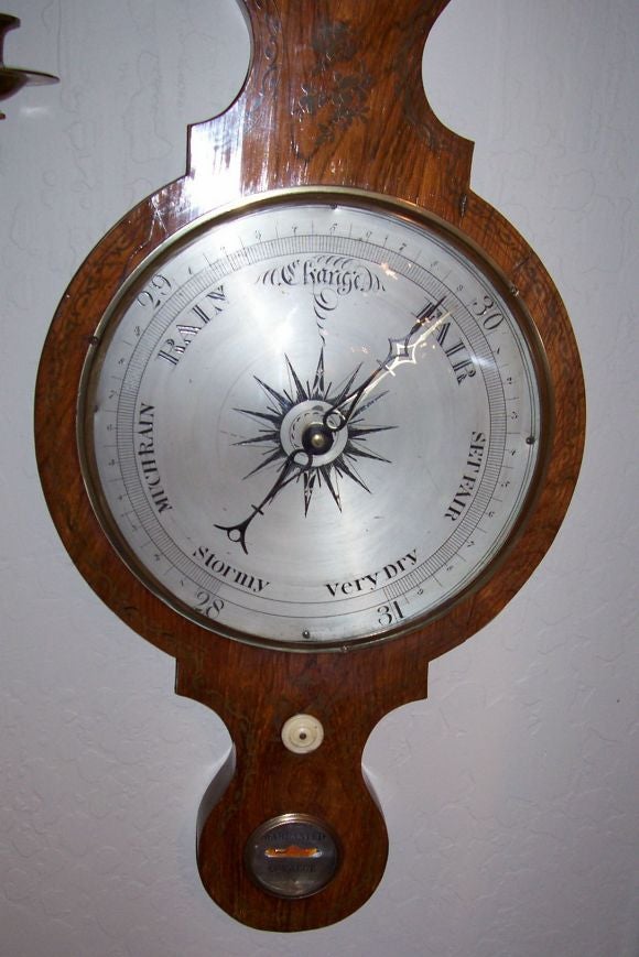 Of typical banjo form, enclosing a hydrometer, thermometer, convex “bull’s eye” mirror within a reeded frame, ten inch dial centering an engraved stylized compass and using an bone knob and a spirit level inscribed: Warranted Correct, beneath a