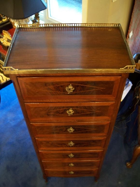 The rectangular top within a pierced three-quarter brass gallery above seven crossbanded drawers with rocaille cast escutcheons and diamond form string inlay, the sides similarly inlaid, above a serpentine apron raised on short cabriole legs.
