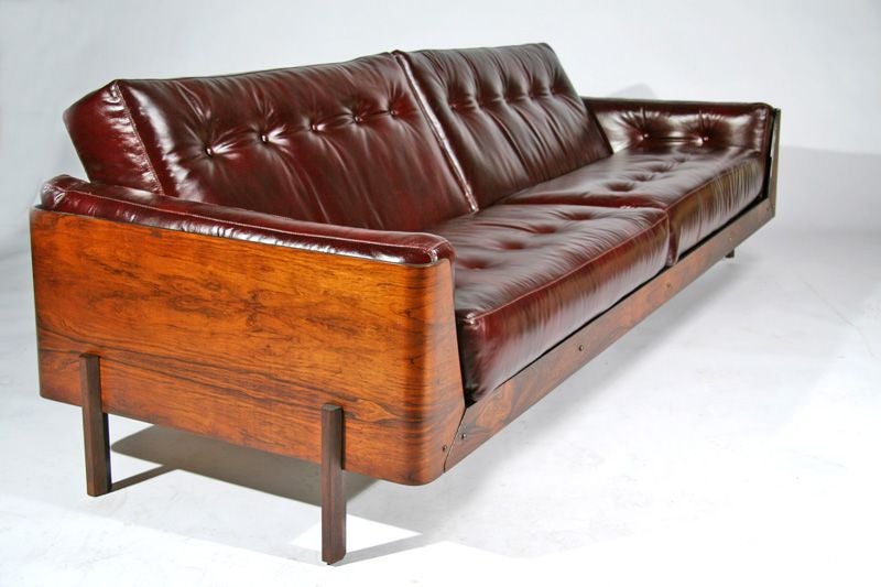 Beautiful rosewood case sofa upholstered in an Oxblood colored leather, with patinated bronze hardware and center leg. Designed for L'Atelier. See also matching pair of lounge chairs listed.  Seat Depth: 21 inches