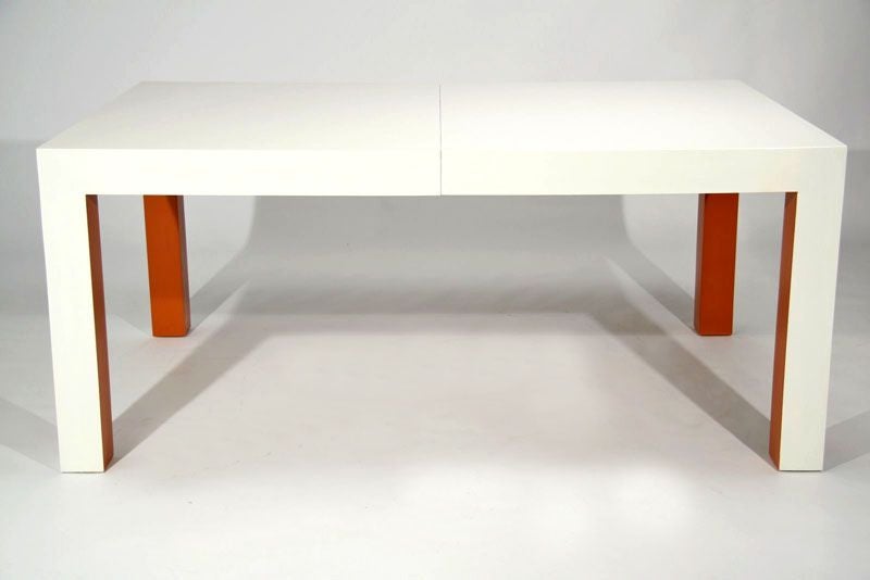 A large parsons style dining table in white lacquer with inset faces of the legs in orange lacquer, designed by Milo Baughman for Thayer-Coggin. Two leaves total; each leaf: 20