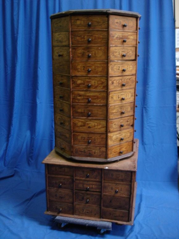 A large Bolt Bin with writting on all the drawers in French with different sizes marked on each. The top revolves and bases has drawers on front and back, paneled on sides. Would serve well as a decoration for a retail store.