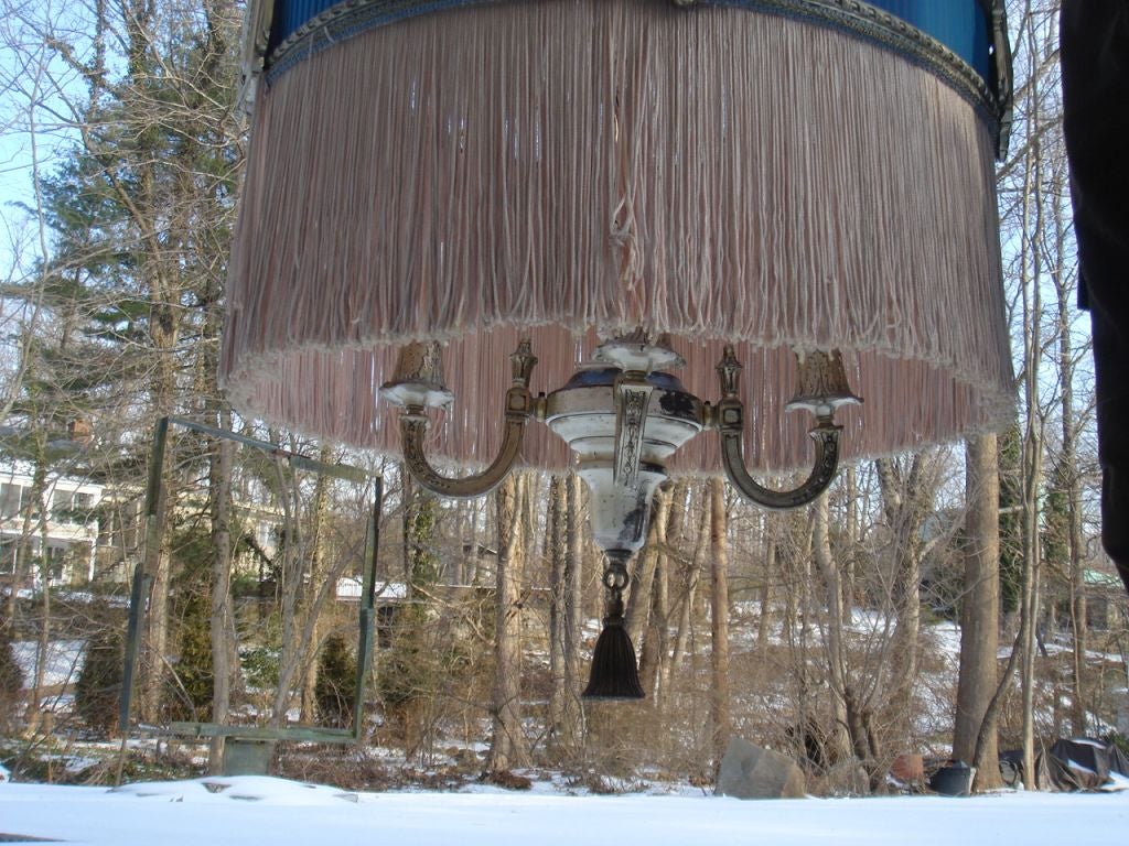 A hanging light with silver-plated metal work of four candelabra hanging from a center stem and fringe shade surround.<br />
<br />
The unrestored sister shade pictured is included.