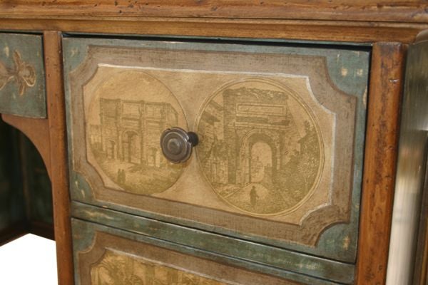 The walnut finish plank top with molded edge supported by a rectilinear body with seven drawers –  one a pencil drawer flanked by six supply drawers with French pastoral scenes in applied decoupage in sepia tones with painted scrollwork borders. The