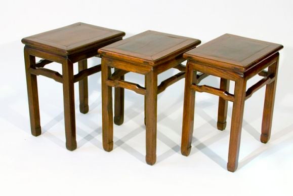 This set of three Huanghuali sidetables with framed inset wood panel and exposed tendons. The humpback high stretcher stabilizes the square section legs with in-turned hoof feet.; wear to finish; discoloration and ring marks on tops.