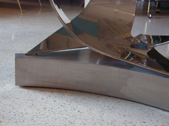 Superb example by Ron Seff, onetime apprentice of Karl Springer, this polished steel dining table is comprised of a triangulated lower support in brushed stainless steel over wood, on top of which rests the sculptural form of a cut and bent square