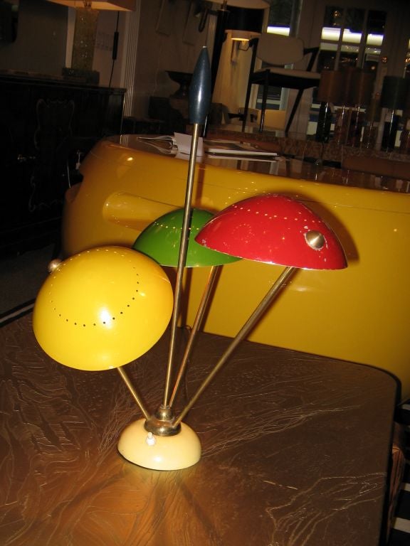 Eine sehr seltene Tischlampe mit einer frühen Version eines Sockels aus cremefarben lackiertem Metall, an dem drei abgewinkelte Messingarme befestigt sind, die jeweils eine Lichtquelle und einen becherförmigen Schirm aus lackiertem Metall tragen.