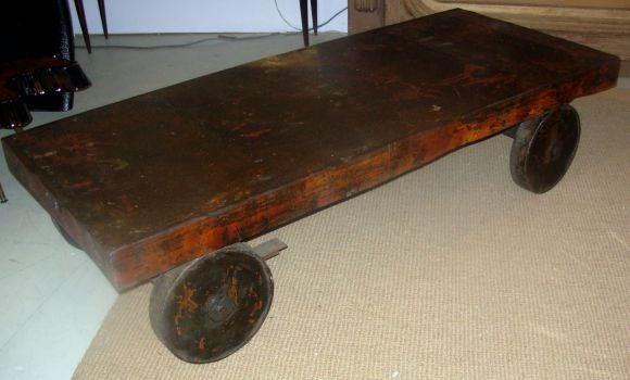 A large industrial cart with remains of orange paint that create a wonderful patina.  The top has bumps and irregularities.